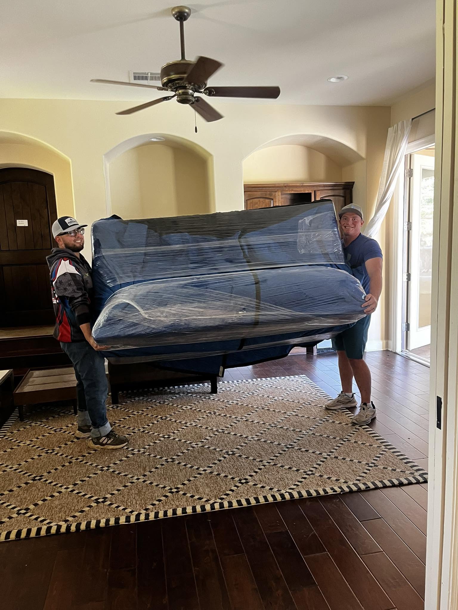 Three Brothers Moving ATX team carefully moving a wrapped sofa